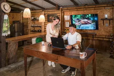 a man and a woman sitting at a table with a laptop at Cabaña Manantial del Turpial in Jardin