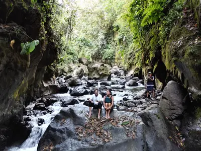 three people sitting on rocks in a stream at Cabaña Manantial del Turpial in Jardin