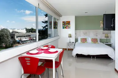 a bedroom with a bed and a table with red chairs at LLanogrande Aparta Estudio Puerto Bulevar in Rionegro