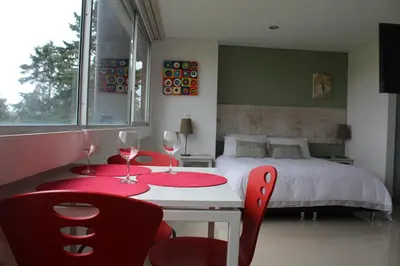 a bedroom with a bed and a table with two red chairs at LLanogrande Aparta Estudio Puerto Bulevar in Rionegro