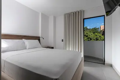 a bedroom with a white bed and a large window at Hotel Balcones del Estadio in Medellín