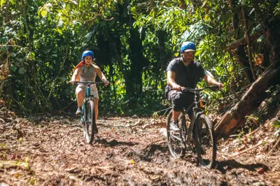 two people riding bikes on a trail in the jungle at El Tigrillo Rio Claro by Los Colores Ecoparque in Doradal