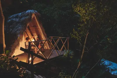 a cabin in the woods at night with a thatch roof at El Tigrillo Rio Claro by Los Colores Ecoparque in Doradal