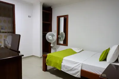 a bedroom with a bed with a green blanket and a fan at Hotel el imperio in Quibdó