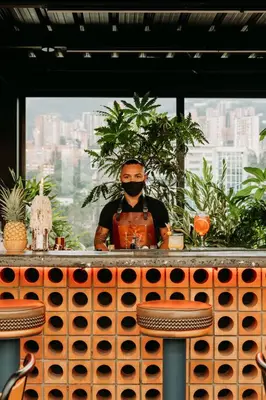 a man wearing a mask behind a bar with wine bottles at The Somos Beats Hotel & Rooftop in Medellín