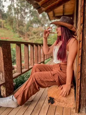 a woman sitting on a wooden porch with a hat at Las Orquídeas EcoHostel in Guarne