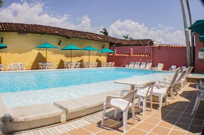 a swimming pool with chairs and tables and blue umbrellas at Casa Hotel Guaracú in Santa Fe de Antioquia