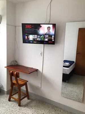 a room with a tv on a wall with a wooden table at Roomies House By Rincon in Medellín
