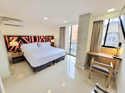 a bedroom with a white bed and a desk and a window at Origen Local Suites in Medellín