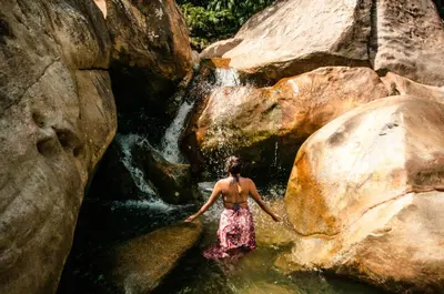 a woman standing in the water next to a waterfall at La Perla Negra - Black Pearl Eco Hostel in San Rafael