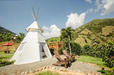 a white teepee with a couple of chairs in front of a mountain at Cerro Tusa Glamping in Titiribí