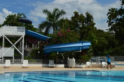 a woman walking by a swimming pool with a blue slide at Apartasol Santa Fe de Antioquia in Santa Fe de Antioquia