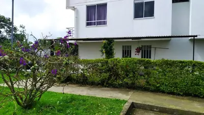 a white house with a hedge and purple flowers at Apartamento-Habitación Palonegro Manizales in Manizales