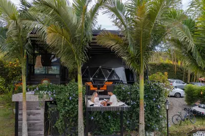 a couple sitting on a balcony of a house with palm trees at Glamping Montecarlo Domo Geodesico y Sauna Finlandés Guatapé in Guatapé