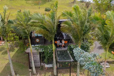 two people sitting on the porch of a house between two palm trees at Glamping Montecarlo Domo Geodesico y Sauna Finlandés Guatapé in Guatapé