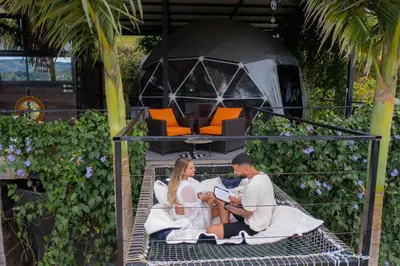 a man and a woman sitting on a bed at Glamping Montecarlo Domo Geodesico y Sauna Finlandés Guatapé in Guatapé