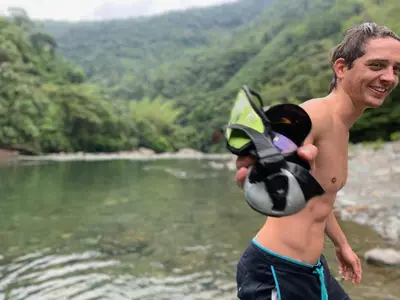 a shirtless man holding a helmet in front of a river at Ecocabaña Pocahontas en rio Santo Domingo, Melcocho in Cocorná