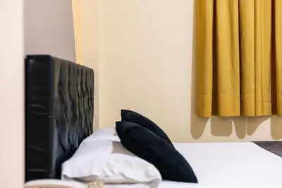 a bed with black and white pillows and a yellow curtain at HOTEL CALLE REAL SUITE in Medellín