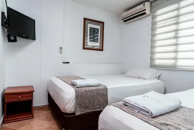 a room with three beds and a tv and avertisement at Hotel Cabo de la Vela Medellin in Medellín