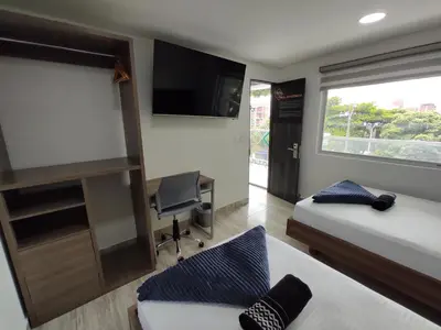a bedroom with two beds and a tv and a chair at Hostel Boutique Nido de Loros in Medellín