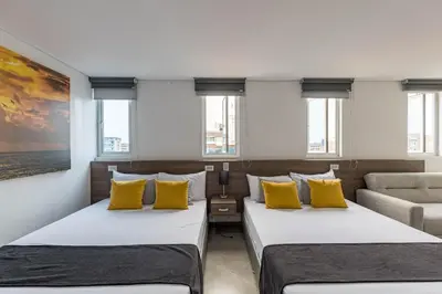 two beds in a room with yellow pillows and a couch at Hotel Velero in San Antonio de Pereira