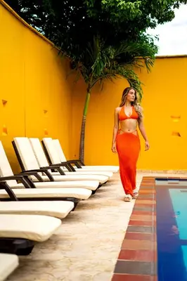 a woman in a orange dress walking by a pool at Curazao Hotel -Centro Histórico- in Santa Fe de Antioquia