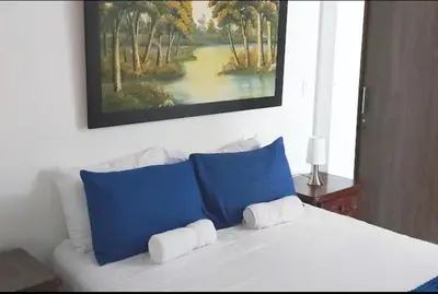 a white bed with blue pillows and a painting on the wall at El EmAnJe 1 in Jardin