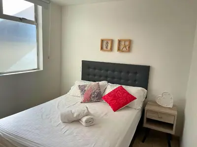 a bedroom with a bed with white sheets and red pillows at Apartamentos Avenida del malecón, frente al lago. Guatape in Guatapé