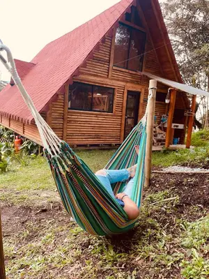 a woman laying in a hammock in front of a log cabin at BRUMA BLANCA CHALETS in Medellín