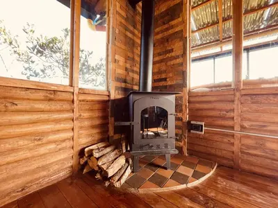 a woodburning stove in a log cabin with windows at Skyline Ecoliving Santa Elena in Santa Elena
