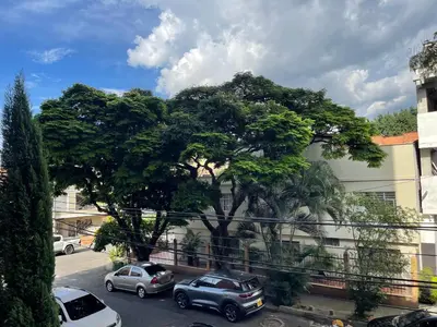 a tree in front of a building with parked cars at En Laureles con ascensor , balcón y muy bien ubicado en laureles Medellín , EL BARRIO MAS COOL DEL MUNDO in Medellín