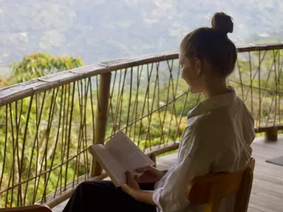 a woman sitting on a balcony reading a book at Ecofinca Fuente Alegre in Cocorná