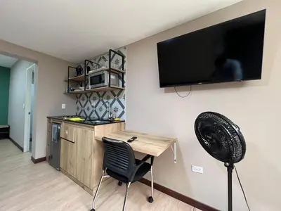 a kitchen with a desk and a television on a wall at Económico alojamiento en Medellín por días - A102 By Roots Rentals in Medellín