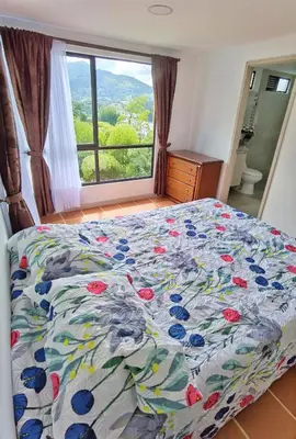 a bed with a floral comforter in a bedroom with a window at Hermosa casa de campo en GUATAPÉ in Guatapé