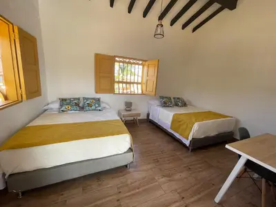a bedroom with two beds and a table and a window at Palmar de Jericó Suites in Jericó