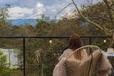 a woman standing on a balcony looking out at the mountains at AKOA GLAMPING Eco-Luxury Hotel in Guarne