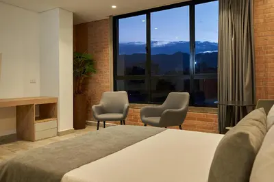 a bedroom with a bed and chairs and a large window at Eutopiq Hotel in Medellín