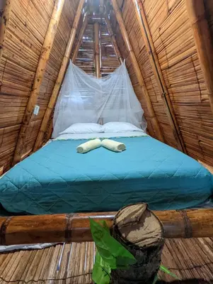 a bed in a bamboo tent with two slippers at Cabañas Camino al Agua - Cocorná in Cocorná