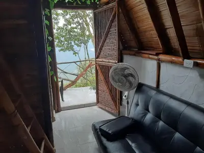 a living room with a black couch and a fan at Cabañas Camino al Agua - Cocorná in Cocorná