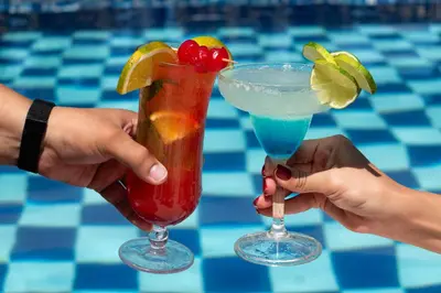 two hands holding two cocktails in front of a pool at Hotel Villa Alicia in San Jerónimo