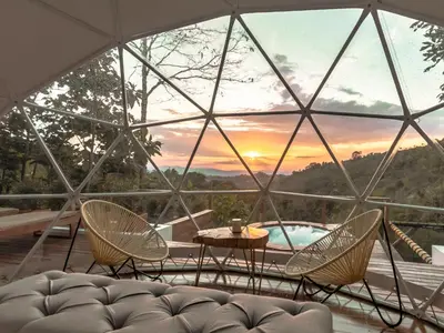 a glass house with a table and chairs and a sunset at Nazca Glamping in Villamaría
