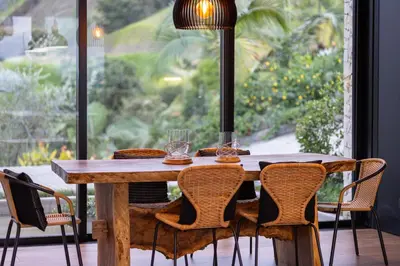 a wooden table with chairs around it with a large window at Villa al lado de la represa de Guatapé con jacuzzi y cancha de tennis privada in El Peñol