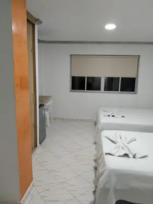 a room with four white beds and a table at Hotel Kariary in Puerto Boyacá