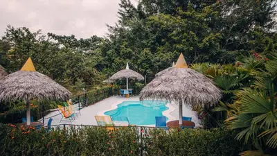 a swimming pool with two straw umbrellas and a swimming pool at Makenke Hostel By Los Colores Ecoparque in Doradal