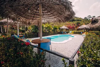 a pool with an umbrella and a table and chairs at Makenke Hostel By Los Colores Ecoparque in Doradal