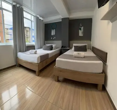 two beds in a room with wooden floors and windows at Hotel Pass, Laureles Medellín in Medellín