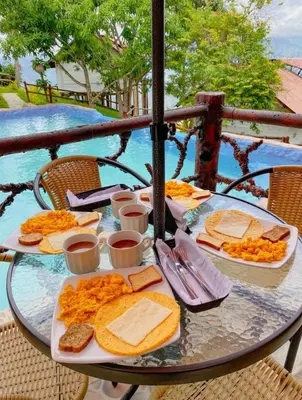 a table with plates of food on a table with a pool at Glamping Mirador Santa Fe-Sopetran in Sopetran