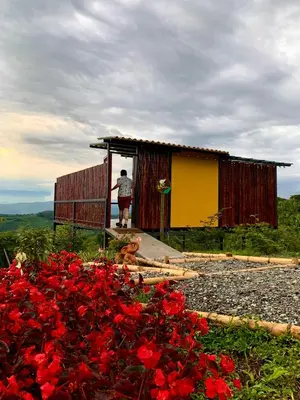 a man standing outside of a small house with red flowers at La Paloma Glamping in Palestina