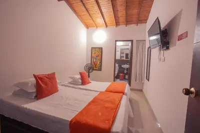 a bedroom with a bed with orange pillows and a television at Hotel Palma De Sevilla Medellin in Medellín