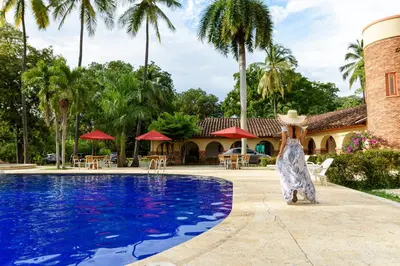 a woman in a hat is standing next to a swimming pool at Finca Hotel Guadalupe in Santa Fe de Antioquia